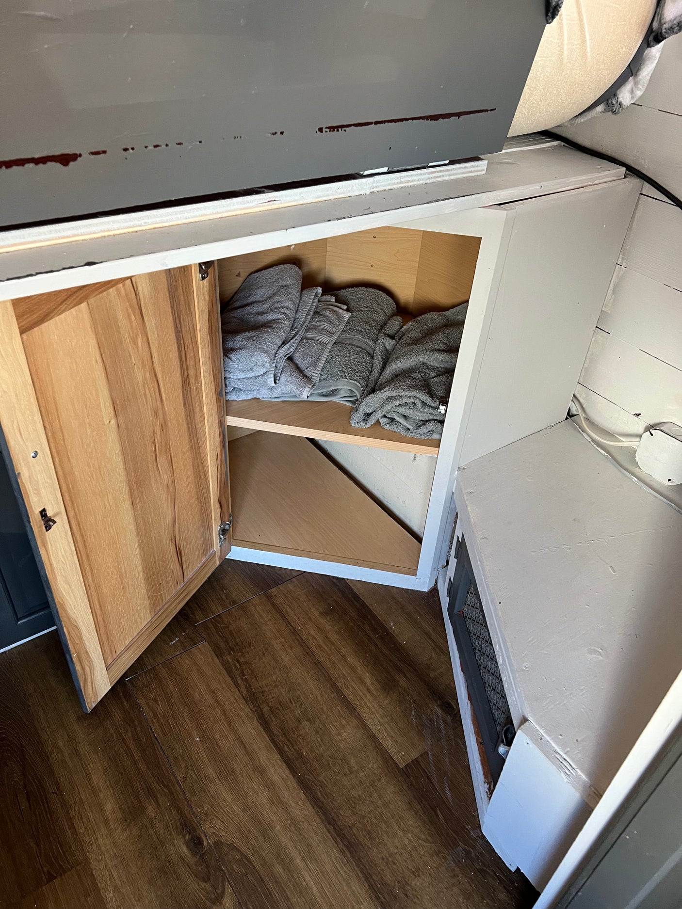 RV rental interior: open cabinet shows neatly folded grey towels, compact storage, and wood floor.