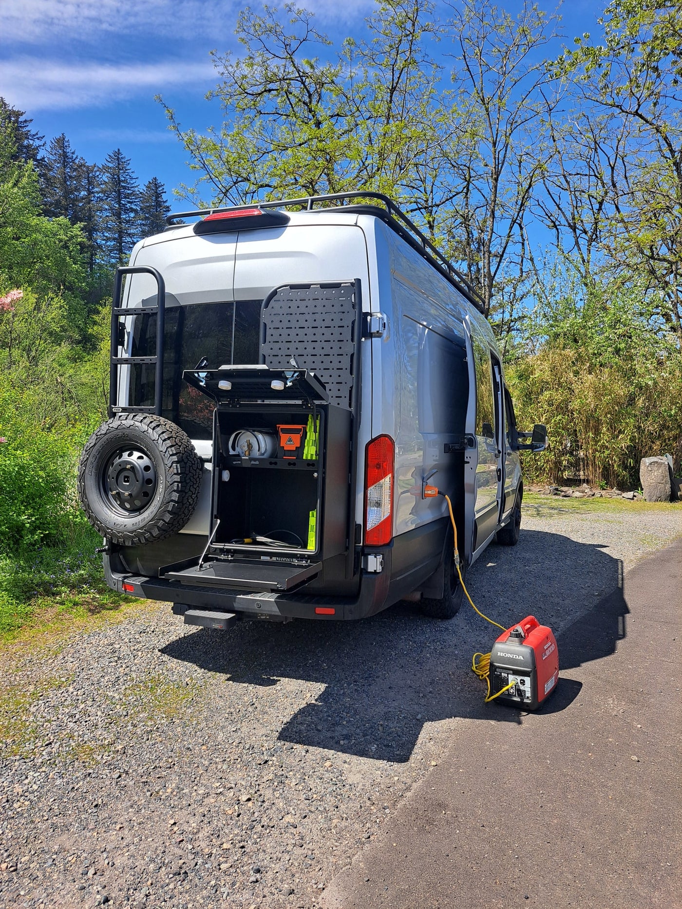 Silver RV rental van with a spare tire and utility rack, connected to a red Honda generator for power. — photo 11