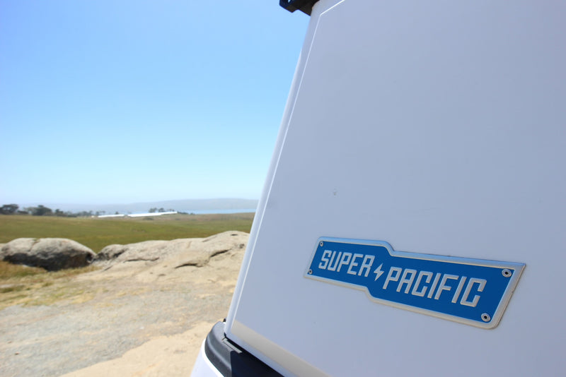 Super Pacific rv rental camper side with its logo, overlooking a scenic landscape of rocks, grass, water, and blue sky. — photo 6