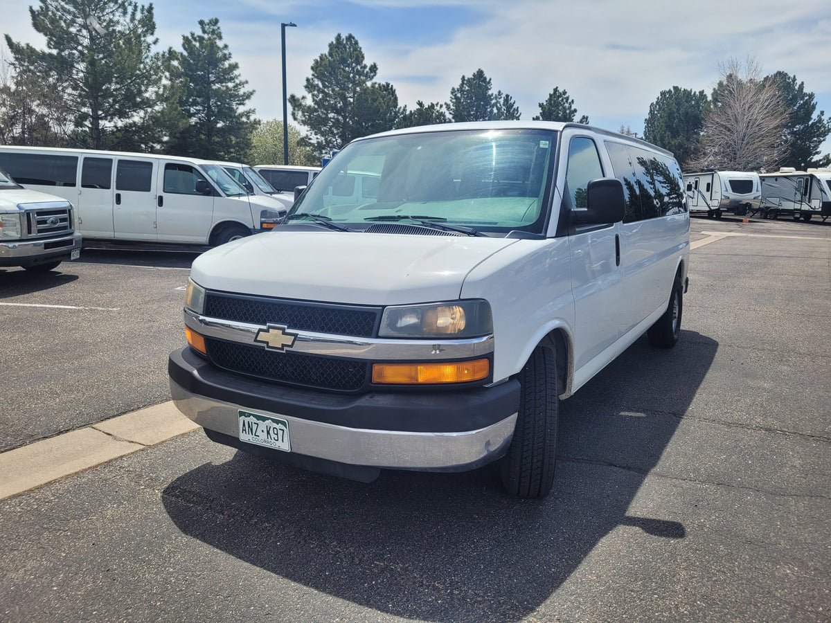 White Chevrolet van parked in an RV rental lot with travel trailers and other vans, ideal for your next trip.