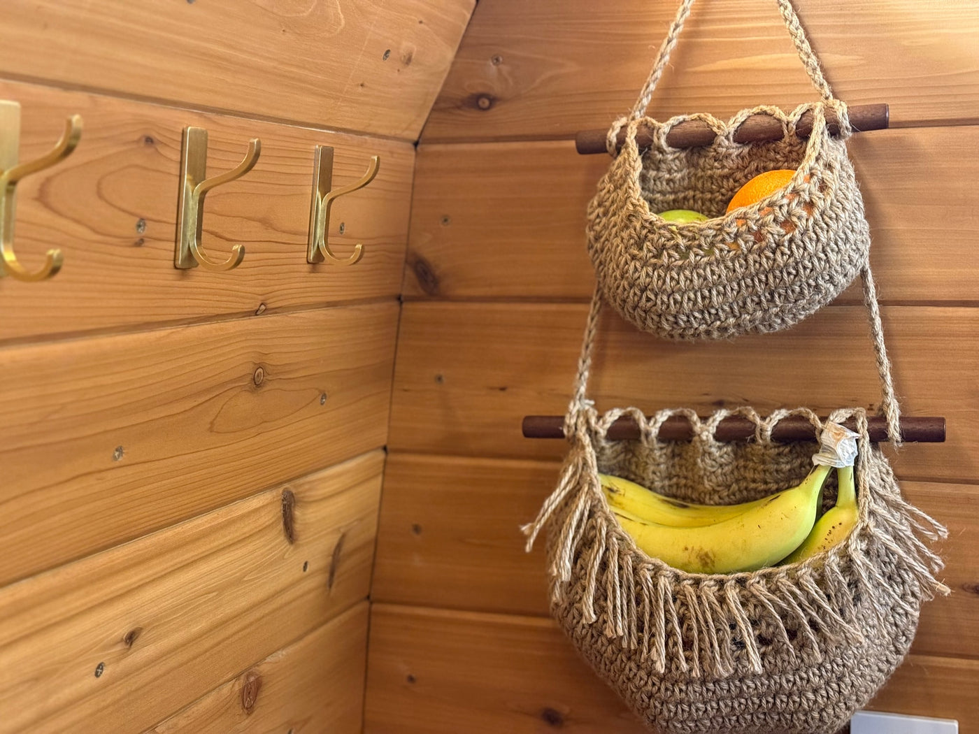 Cozy rv rental interior: wooden walls, brass hooks, and two crocheted baskets holding fruit. Organized storage for your travels. — photo 10