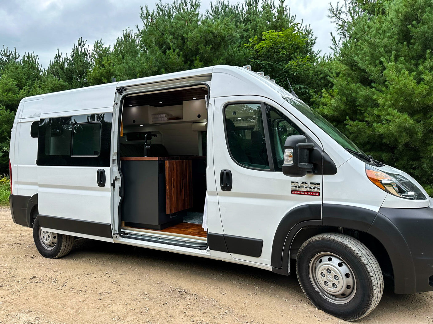 White Ram ProMaster camper van for rv rental, parked outdoors with open side door revealing custom interior.