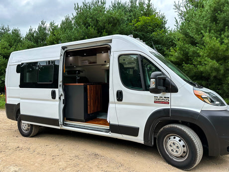 White Ram ProMaster camper van for rv rental, parked outdoors with open side door revealing custom interior.