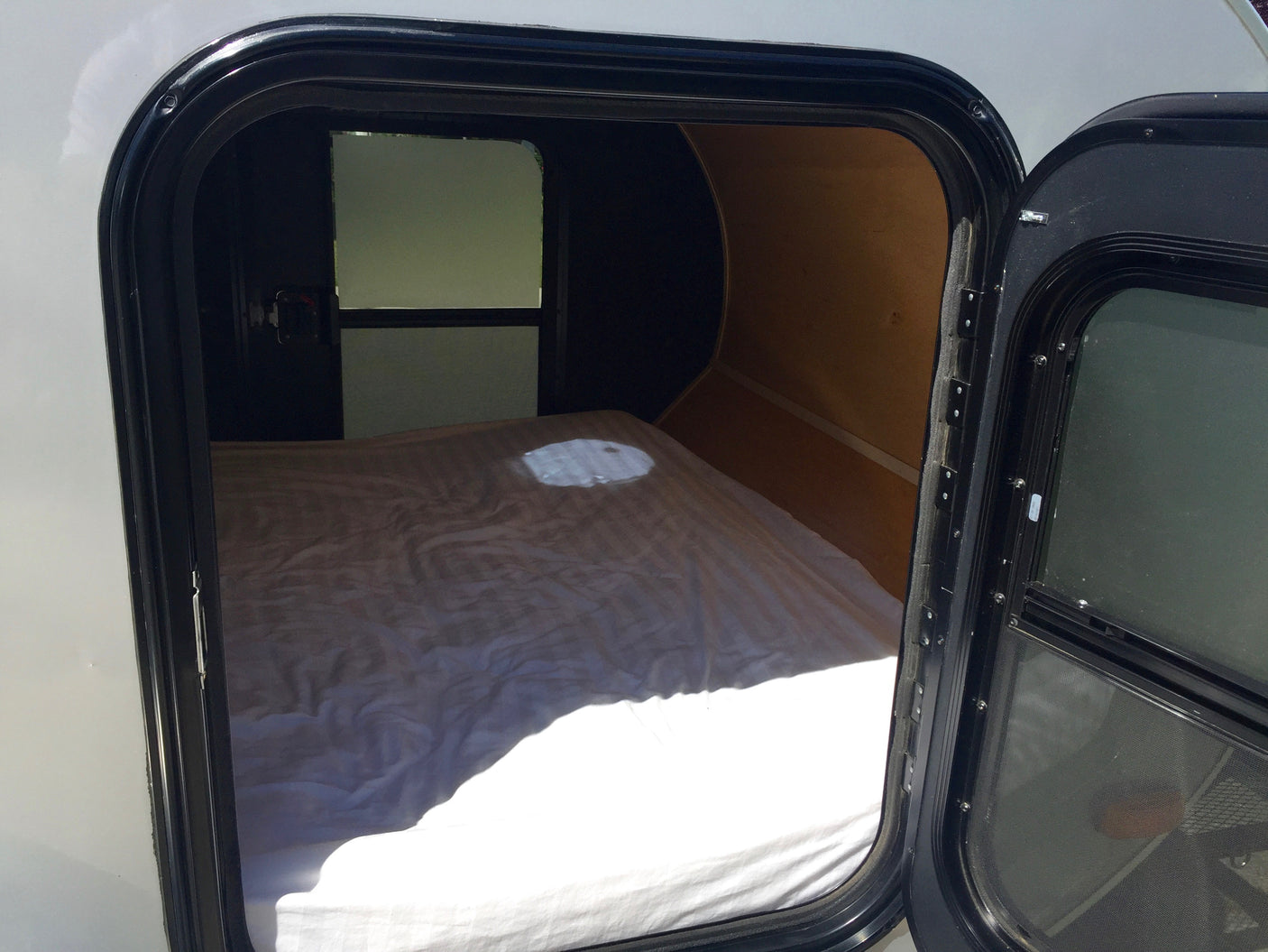 Bright interior of an rv rental camper, showing a made bed and rear window through an open side door.