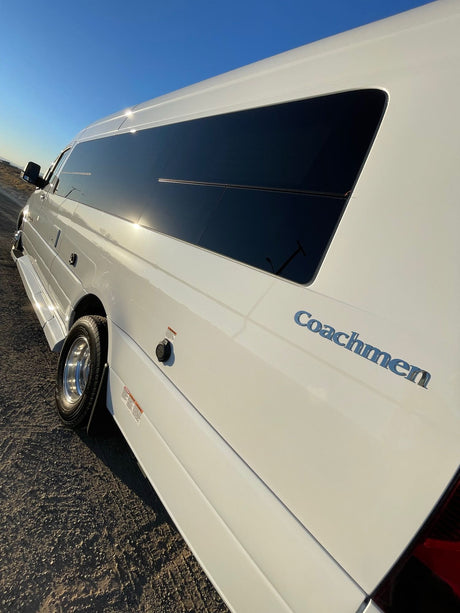 White Coachmen camper van, an ideal RV rental, sparkling on a sunny gravel road under a clear blue sky.