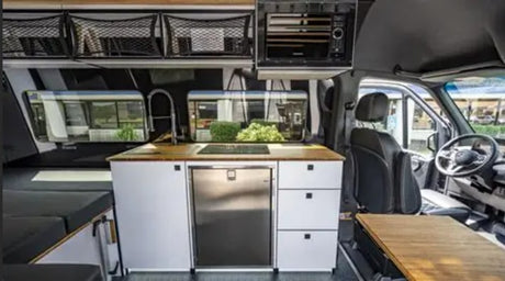 Inside a premium rv rental: compact kitchen with sink, stove, fridge, and comfortable living area with storage.