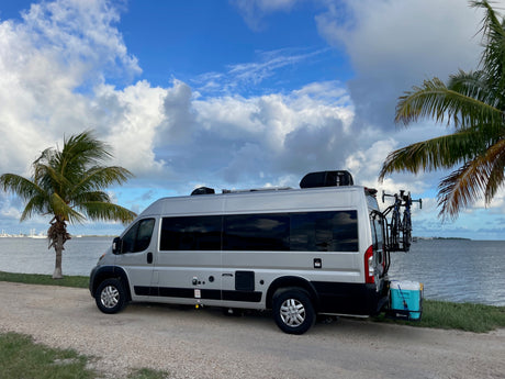 Silver RV rental by tropical water with bikes, cooler, & palm trees. Ideal for adventures!