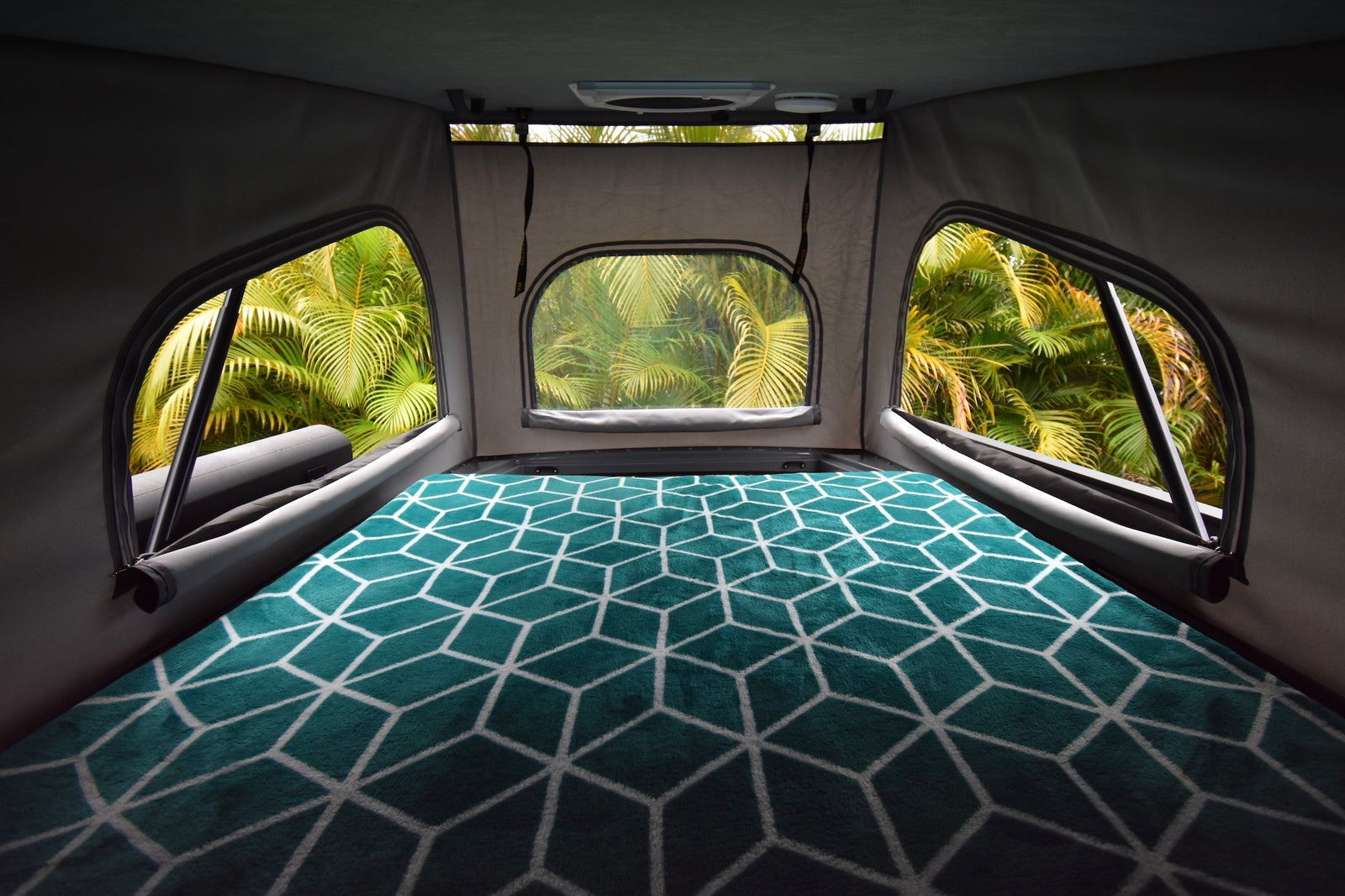 Inside an RV rental, a comfy bed faces lush tropical views through windows. Your cozy travel escape.