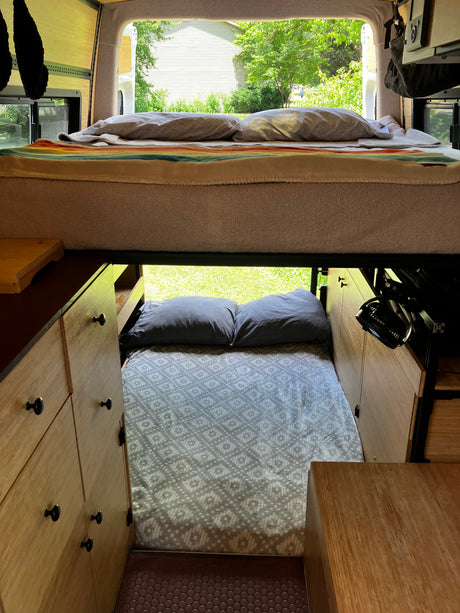RV rental interior shows cozy bunk beds & wood cabinets, with a view of nature outside.