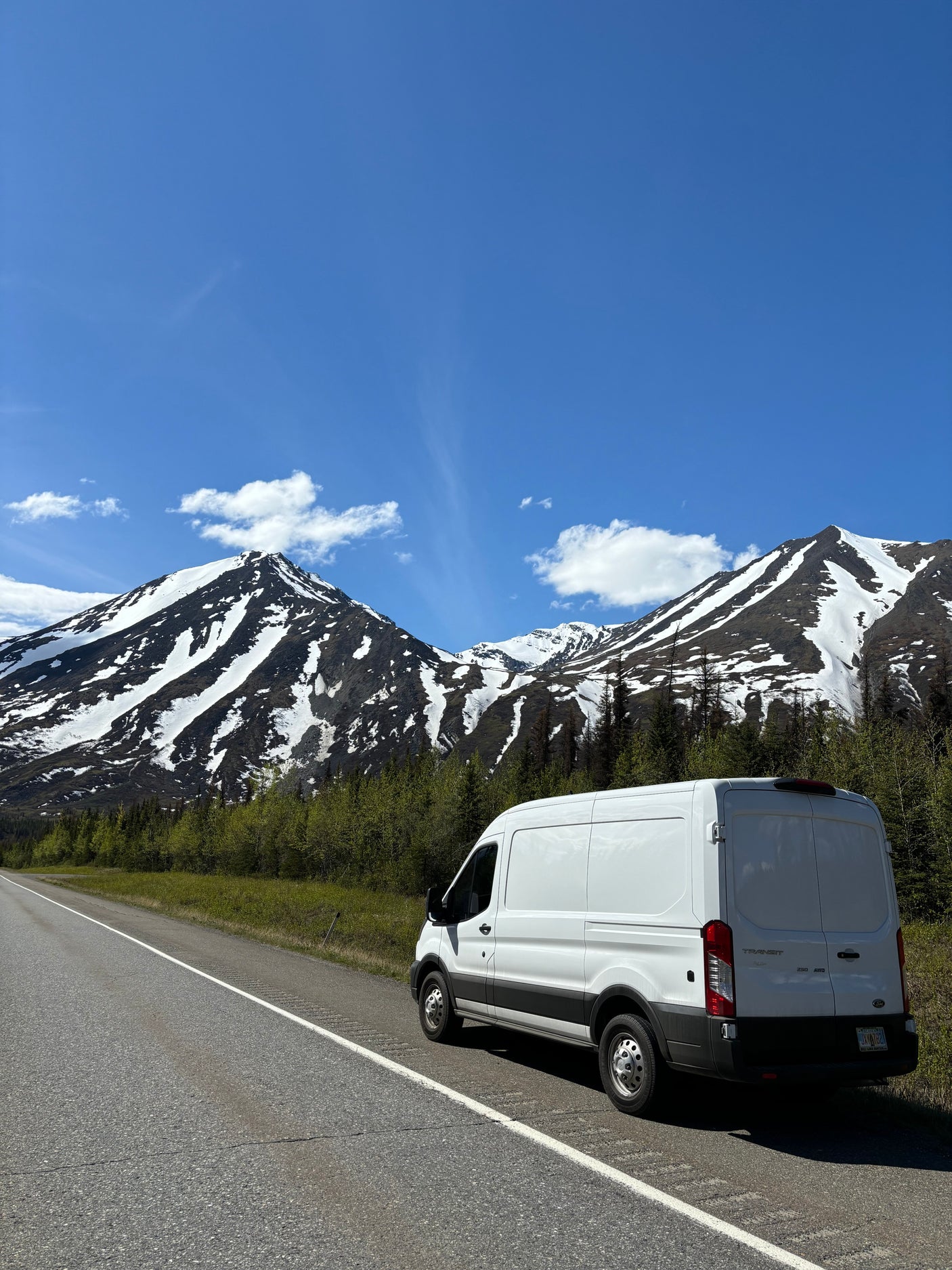 Exploring nature with an RV rental: White van on a scenic mountain road under a bright blue sky.