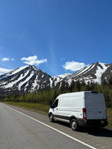 Exploring nature with an RV rental: White van on a scenic mountain road under a bright blue sky.