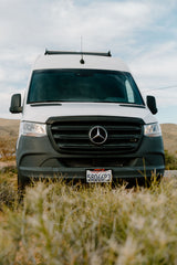 Front view of a white Mercedes Sprinter van, common as an RV rental, parked in an outdoor setting. CA plate 58066P3.
