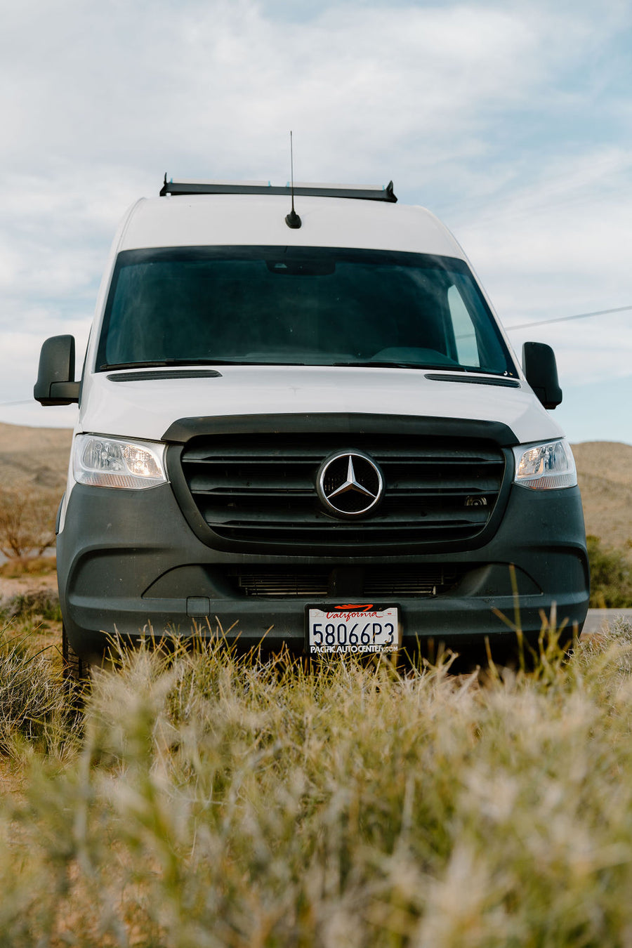 Front view of a white Mercedes Sprinter van, common as an RV rental, parked in an outdoor setting. CA plate 58066P3.