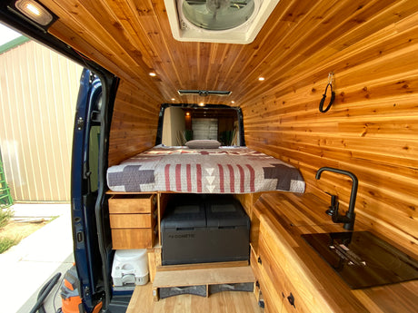 RV rental ready: Beautifully crafted camper van interior with wood paneling, bed, kitchen, Dometic fridge, and toilet.