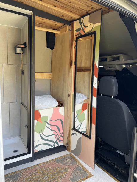 RV rental van conversion with a compact shower, cozy sleeping area, and colorful custom interior design, including a mirrored door.
