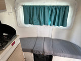 Cozy RV rental interior with teal curtains, bench seating, and compact kitchenette for travel, offering a comfortable space.