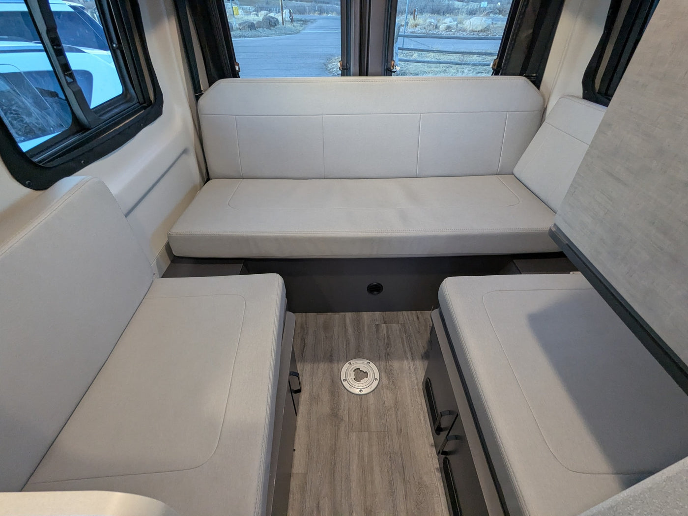 Comfortable RV rental interior with light gray padded seating, wood-look floor, and large windows revealing an outdoor scene. — photo 6
