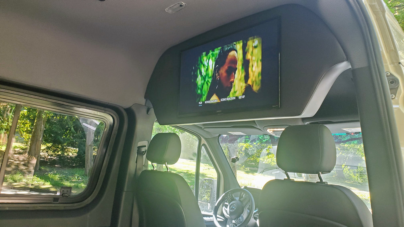 RV rental interior: A ceiling TV plays a movie, with the front seats and outside nature visible through the windows.