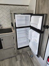 Modern RV rental kitchen showcasing an open, empty two-door refrigerator, ready for your camping food. Features sleek wood finishes.