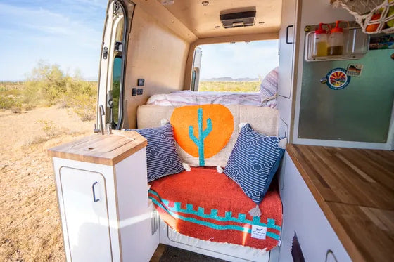 Cozy RV rental interior with desert view. Features a functional kitchenette, comfy seating, and bed for your next adventure.