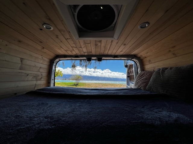 Cozy RV rental interior with bed & wood paneling. Stunning view of turquoise water, blue sky, & coastal trees. Perfect travel!