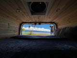 Cozy RV rental interior with bed & wood paneling. Stunning view of turquoise water, blue sky, & coastal trees. Perfect travel!