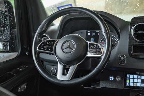 Inside a modern Mercedes-Benz RV rental: a detailed view of the steering wheel and dashboard controls, ready for adventure.