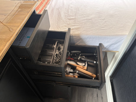 RV rental kitchen: Three open, organized drawers containing kitchen utensils, a guide, and clips. Compact storage.