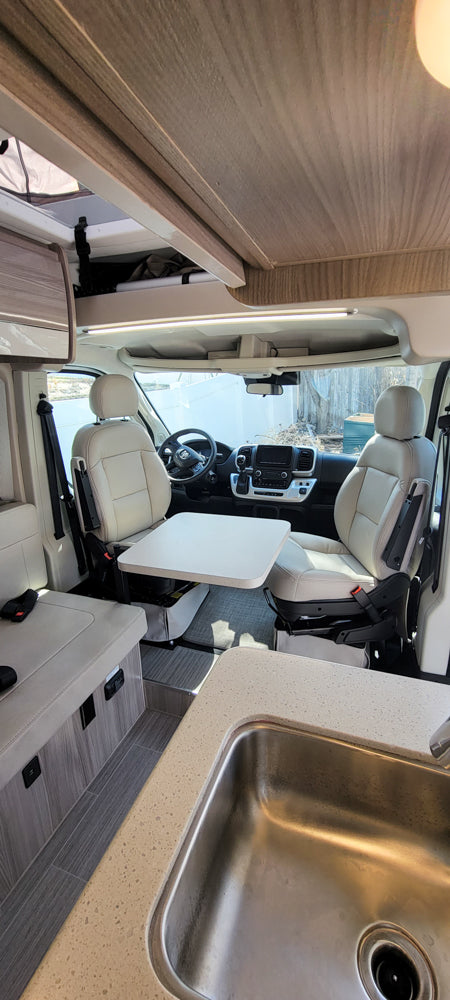 Bright rv rental interior featuring cream seating, a flexible dining table, and a functional kitchen area with a sink.