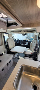 Bright rv rental interior featuring cream seating, a flexible dining table, and a functional kitchen area with a sink.