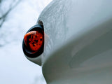 Close-up of an orange side marker light on a white vehicle, likely an RV, reflecting tree branches. Essential for any rv rental.