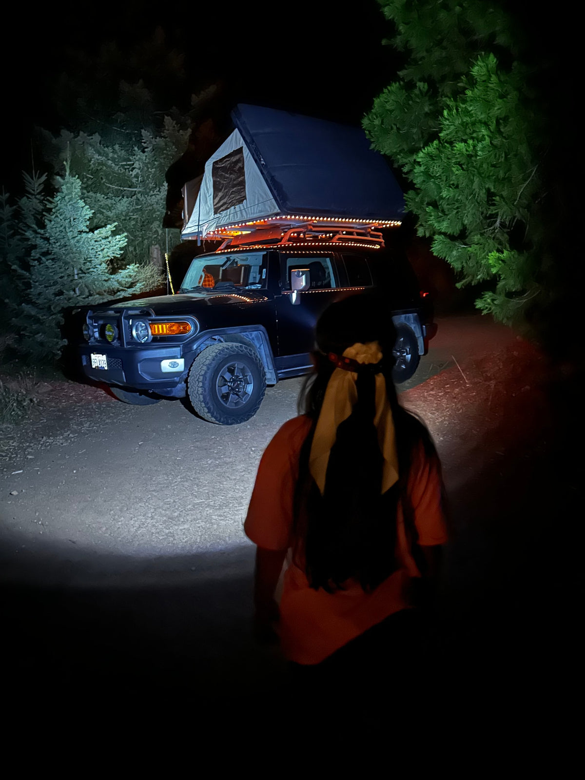 Adventure awaits! An RV rental (SUV with a rooftop tent) set up for night camping with string lights. A person walks closer. — photo 20