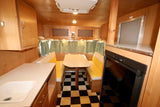 Cozy rv rental interior featuring wood paneling, a dinette with yellow benches, kitchen counter, and checkered floor.