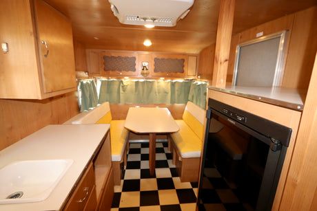 Cozy rv rental interior featuring wood paneling, a dinette with yellow benches, kitchen counter, and checkered floor.