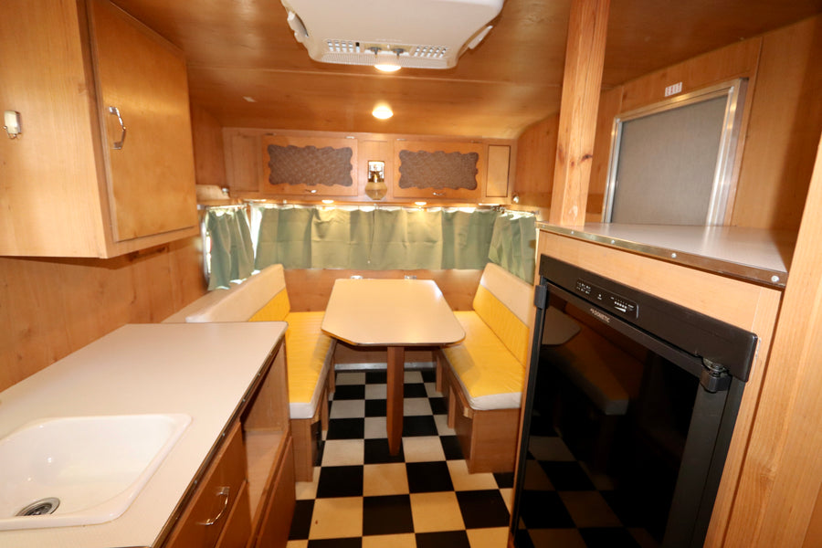 Cozy rv rental interior featuring wood paneling, a dinette with yellow benches, kitchen counter, and checkered floor.