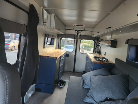 Inside a modern **rv rental**: a compact kitchen with wood counters, comfortable sofa bed, and ample storage for van life.