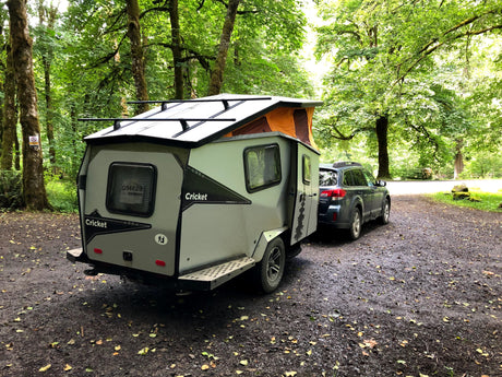 Explore nature with this Cricket compact camper trailer, perfect for **RV rental** adventures, hitched to a Subaru in a lush forest setting.