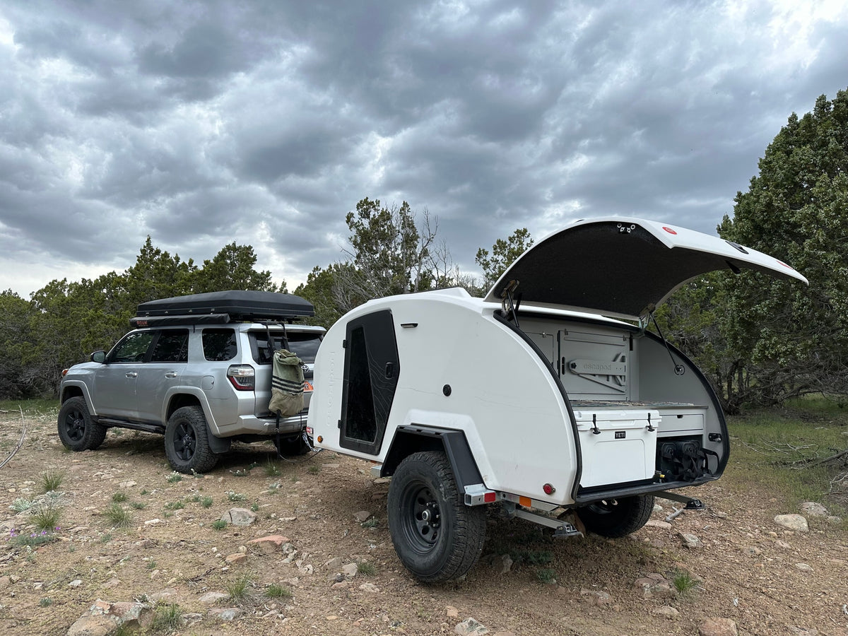 A silver SUV with a rooftop tent tows a white teardrop RV rental