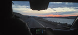 Scenic RV rental road trip at sunset. View from inside, highway stretching alongside a river with distant wind turbines.