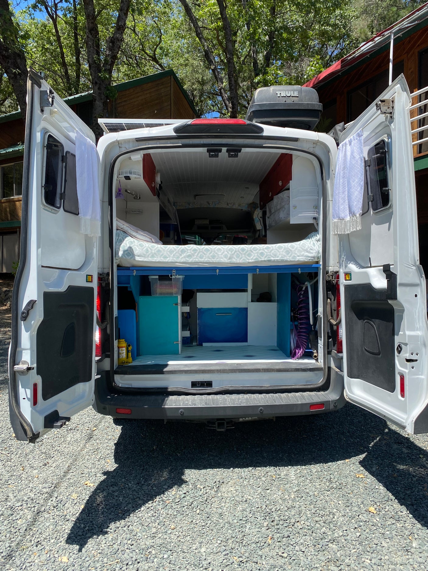 Open rear doors of a white camper van reveal a custom interior with bed & kitchen, perfect for an rv rental adventure.
