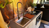 Modern RV rental kitchen: sleek sink, induction cooktop, microwave, and stylish metal backsplash.