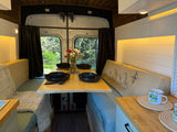 Charming RV rental interior: a cozy dinette with table set for four, fresh flowers, and natural window views.