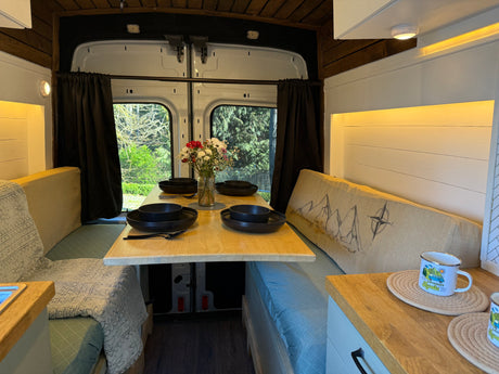 Charming RV rental interior: a cozy dinette with table set for four, fresh flowers, and natural window views.