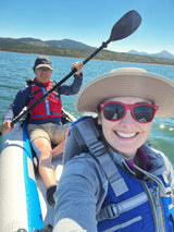 Two people in an inflatable kayak on a sunny mountain lake. A perfect stop for an RV rental adventure! Life vests worn for safety.