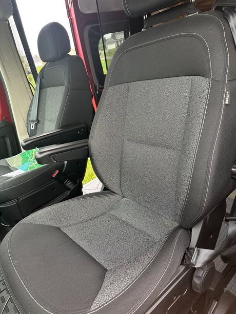 Inside an RV rental: Comfortable black & gray front seats with armrests, white stitching, and visible airbag tags.