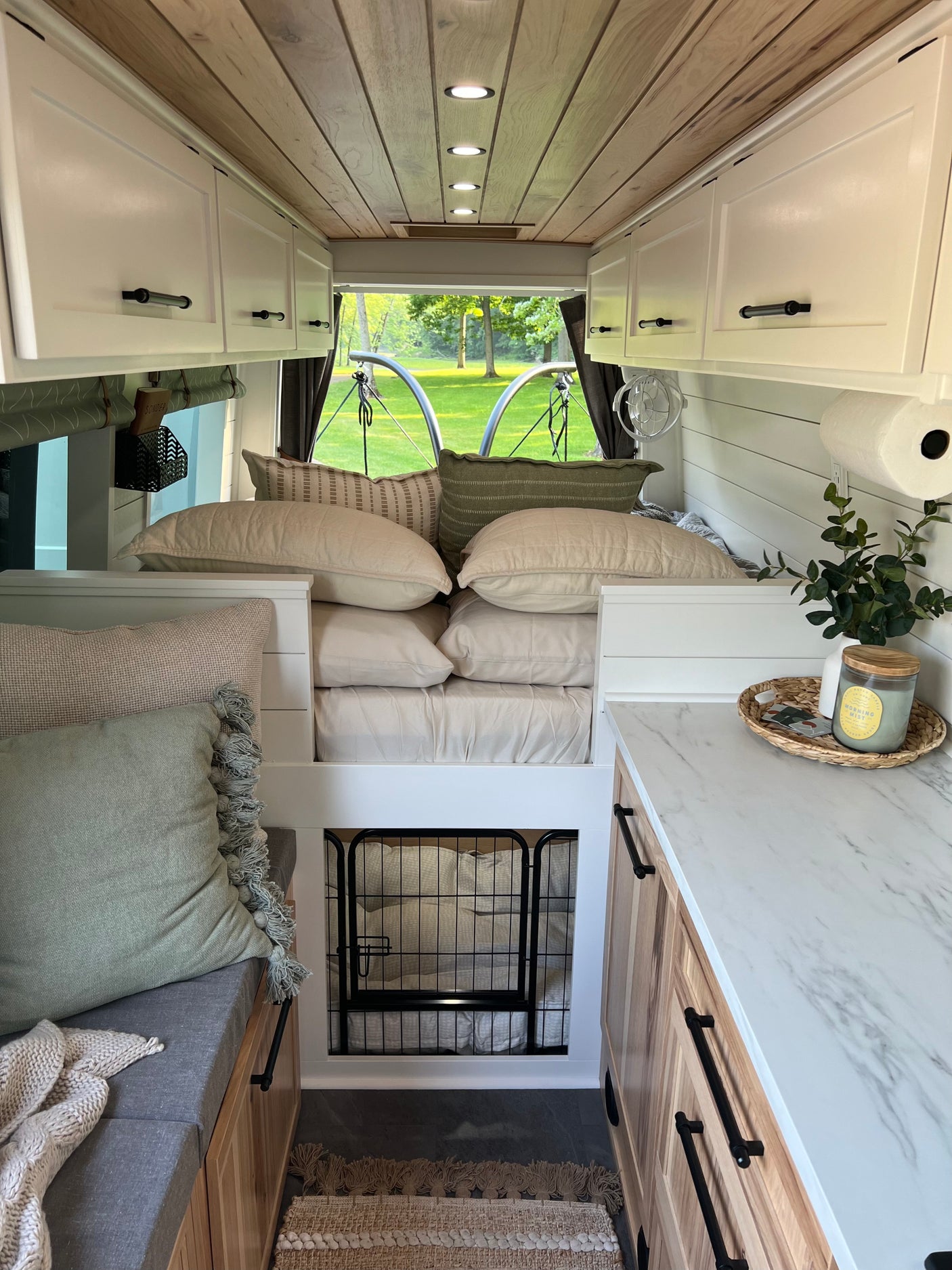 Explore this stylish RV rental interior with a cozy bed, white cabinets, modern wood ceiling, & dedicated pet space.