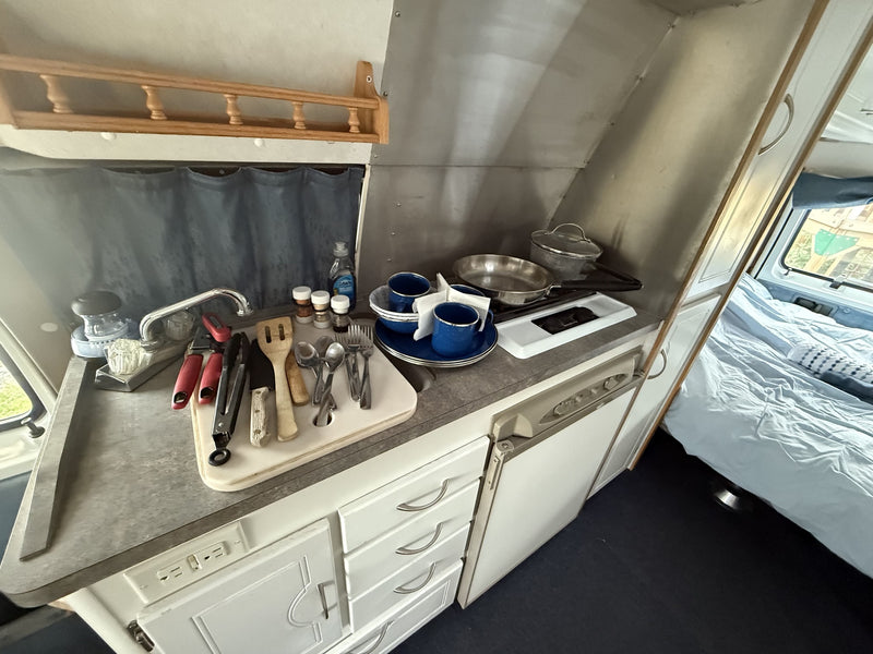 RV rental: functional kitchen setup with sink, utensils, cookware, compact fridge, and adjacent bed area. — photo 5