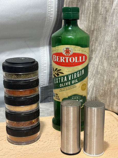 RV rental cooking kit: Bertolli olive oil, stacked spices, and salt/pepper shakers on a wooden board.