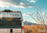 Adventure awaits! Vanish RV rental parked in a sunlit desert, backed by mountains and sparse plants under a blue sky.
