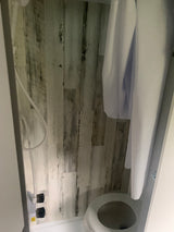 RV rental: Compact wet bath with toilet, shower hose, and white curtain against rustic wood-look walls.